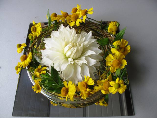 The low glass bowl is filled with curly willow yellow heleniums and one 